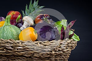 FRESH AND ORGANIC VEGETABLES AND FRUITS IN WOVEN BASKET ISOLATED ON BLACK BACKGROUND