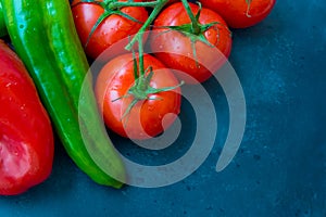 Fresh organic vegetables, tomatoes on a vine, green italian and red bell peppers, dark blue background, styled image, top view