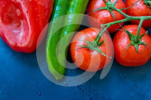 Fresh organic vegetables, tomatoes on a vine, green italian and red bell peppers, water drops, dark blue background, styled image