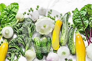 Fresh organic vegetables - zucchini, squash, cucumbers, broccoli, onions, garlic, chard, green peas on a light background, top vie