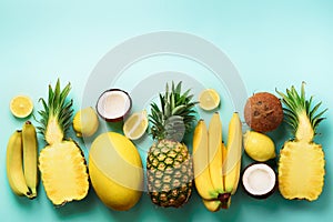 Fresh organic yellow fruits over blue background. Monochrome concept with banana, coconut, pineapple, lemon, melon. Top