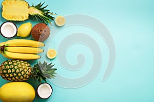 Fresh organic yellow fruits over blue background. Monochrome concept with banana, coconut, pineapple, lemon, melon. Top
