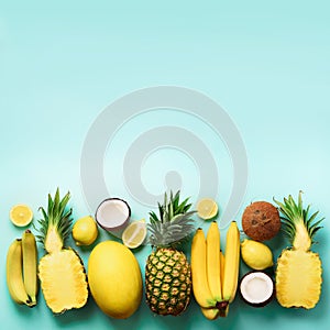 Fresh organic yellow fruits over blue background. Square crop. Monochrome concept with banana, coconut, pineapple, lemon
