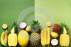 Fresh organic yellow fruits over green background. Monochrome concept with banana, coconut, pineapple, lemon, melon. Top