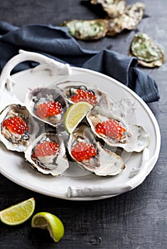 Fresh oysters, garnished with red caviar and lime. Served on a white platter