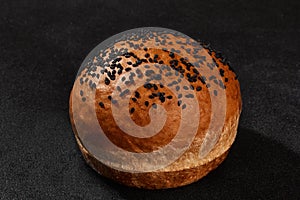 Fresh, palatable baked bun sprinkled with sesame seeds against black background with copy space. Rural cuisine or bakery