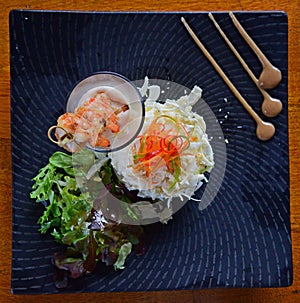 Fresh Palm Salad with Prawn Skewers in a glass on a black square plate with top down view