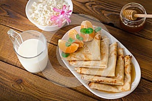 Fresh pancakes with honey, maple syrup, cottage cheese and tangerines. Wooden background. Top view