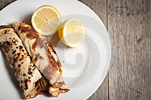 Fresh pancakes with organic lemon seen against a wooden textured background