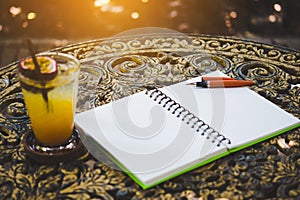 Fresh passion fruit juice in glass on table with is tree garden background, notepad and pen