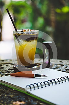 Fresh passion fruit juice in glass on table with is tree garden background, notepad and pen