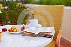 Fresh pastries, coffee, jam, and an open book are arranged on the table. Breakfast on the terrace with an interesting book