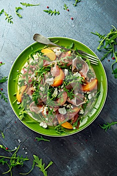 Fresh Peach salad with Parma ham, feta cheese and vegetables in a green plate. healthy food