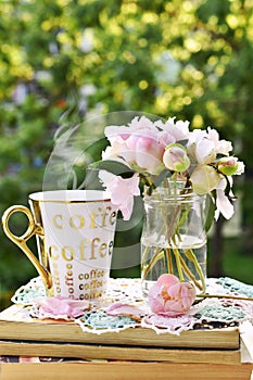 Fresh peonies in glass jar and a cup of hot coffee in the garden