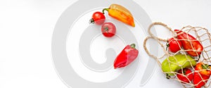 Fresh peppers in string bag on white background. Eco mesh with colorful vegetables. Banner with copy space, top view, flat lay.