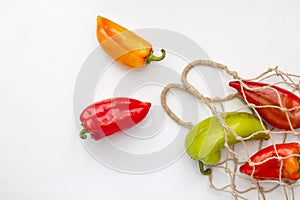 Fresh peppers in string bag on white background. Eco mesh with colorful vegetables, copy space, top view, flat lay. Ecology and