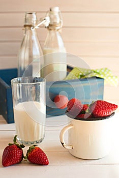 Fresh picked strawberrys with glass of the milk on white wooden background.