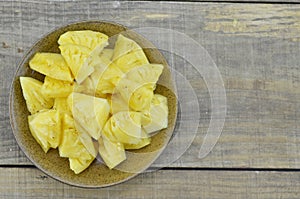 Fresh pieapple cut slices in brown plate on wooden table