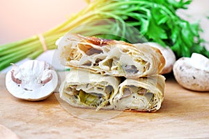 .Fresh piece of savory strudel stuffed with  leek and mushrooms served on a wooden plate,with mushrooms and parsley