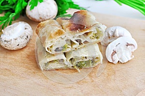 .Fresh piece of savory strudel stuffed with  leek and mushrooms served on a wooden plate,with mushrooms and parsley