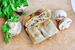 .Fresh piece of savory strudel stuffed with  leek and mushrooms served on a wooden plate,with mushrooms and parsley