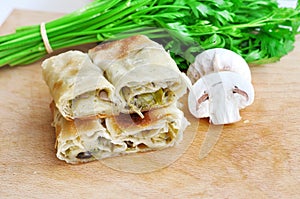 Fresh piece of savory strudel stuffed with  leek and mushrooms served on a wooden plate,with mushrooms and parsley