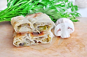 Fresh piece of savory strudel stuffed with  leek and mushrooms served on a wooden plate,with mushrooms and parsley