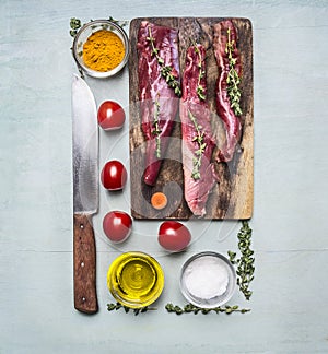 Fresh pieces of raw lamb on a chopping board, with herbs, spices, cherry tomatoes, lined rectangle on wooden rustic background top