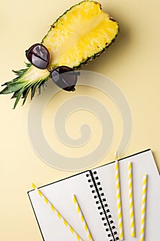 Fresh pineapple cut in two part, notebook or sketchbook and sunglasses on yellow background. Summer concept.