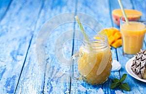 Fresh pineapple and mango smoothie in two glasses with fruits on a blue wooden rustic background