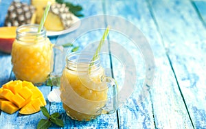 Fresh pineapple and mango smoothie in two glasses with fruits on a torquise wooden rustic background