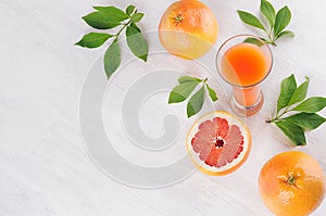 Fresh pink juice and grapefruits with green leaves on white wood board, top view, border.