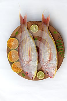 fresh Pink Perch (thread finned Bream) Decorated with lemon slice Orange slice and curry leaves on a wooden pad.