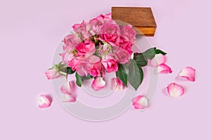 Fresh pink roses in a wooden box on a pink background. Flying rose petals. View from above