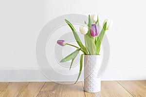 Fresh pink tulip bouquet on a shelf in front of a white wall. View with copy space