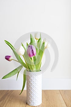 Fresh pink tulip bouquet on a shelf in front of a white wall. View with copy space