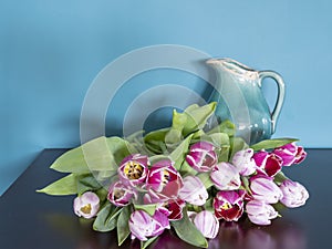Fresh pink tulip flowers bouquet on a old brown table in front of a green wall. View with copy space and shadow