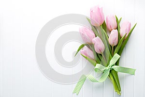 Fresh pink tulip flowers bouquet on shelf in front of wooden wall.