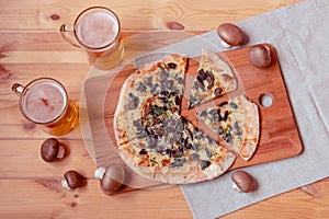 Fresh pizza with cheese and mushrooms and two mugs of beer on wooden table. Top view