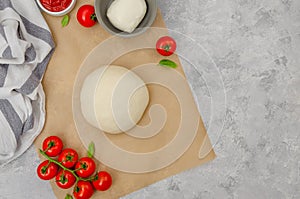 Fresh pizza dough with tomato sauce, mozzarella, tomatoes and basil leaves on a gray concrete background. Italian cuisine.