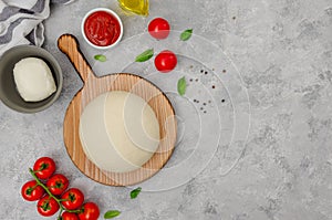 Fresh pizza dough with tomato sauce, mozzarella, tomatoes and basil leaves on a gray concrete background. Italian cuisine.