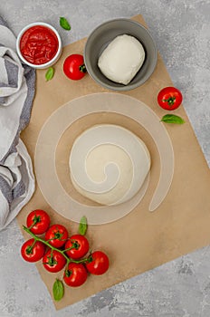 Fresh pizza dough with tomato sauce, mozzarella, tomatoes and basil leaves on a gray concrete background. Italian cuisine. Copy