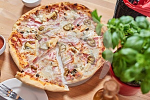 Fresh pizza with ham, hot pepper and capers and black olives on wooden table in restaurant.