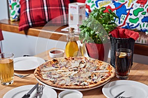 Fresh pizza with ham, hot pepper and capers and black olives on wooden table in restaurant.