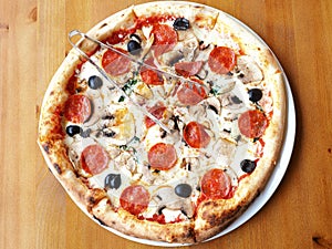 Fresh pizza with mushrooms, sausage and olives stands on a wooden table. Top view