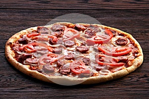 Fresh pizza with tomatoes, cheese, onions and sausage on wooden table closeup