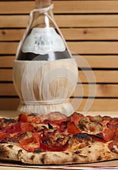 Fresh Pizza on Wooden Table at Restaurant With Bottle of Chianti Wine in Background