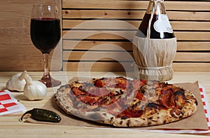 Fresh Pizza on Wooden Table at Restaurant With Bottle of Chianti Wine in Background