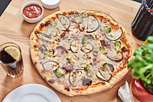 Fresh pizza with with zucchini, dried tomatoes, broccoli and mushrooms on wooden table in restaurant.