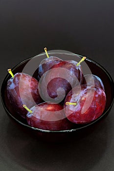 Fresh plum. Autumn harvest. Ripe purple plums in glass bowl on dark background. Concept: seasonal fruits, healthy food. Top view.